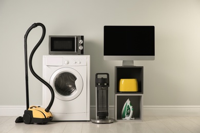 Photo of Modern vacuum cleaner and different household appliances near light wall indoors