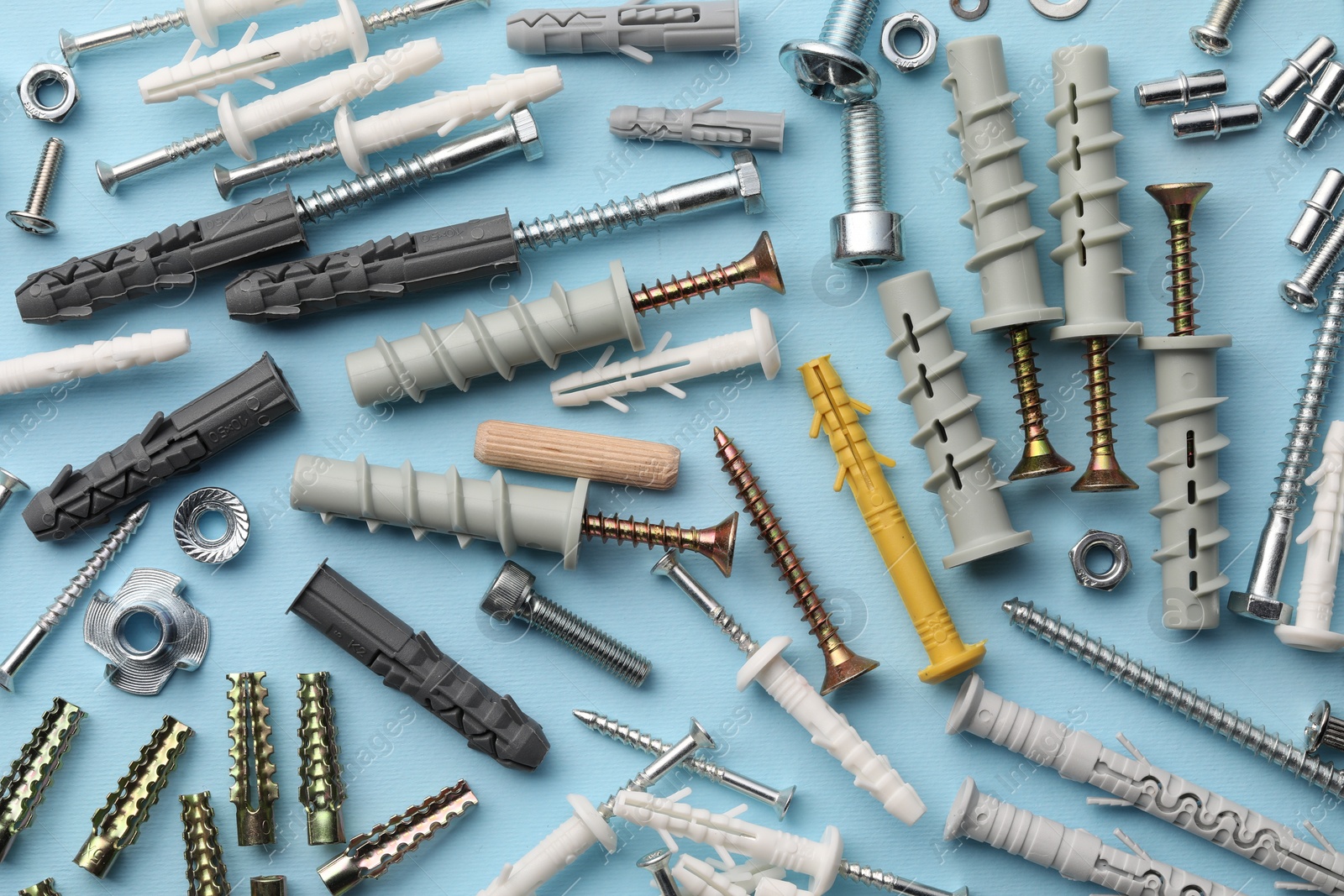 Photo of Many different fasteners and dowels on light blue background, flat lay