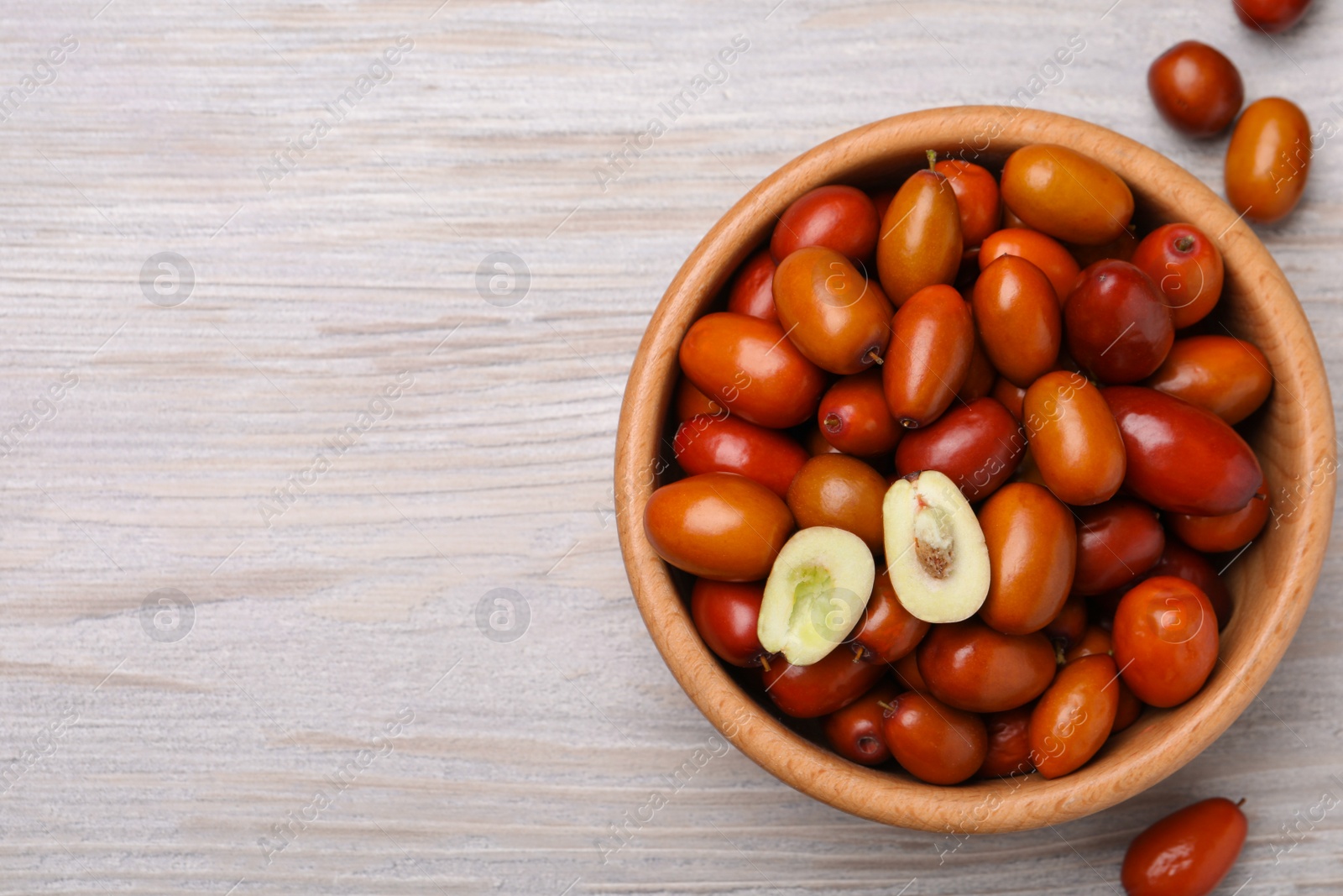 Photo of Fresh Ziziphus jujuba fruits with bowl on wooden table, Flat lay. Space for text