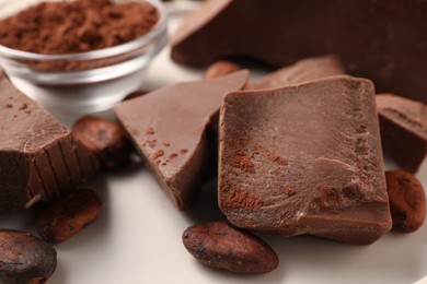 Photo of Pieces of tasty milk chocolate and cocoa beans on white table, closeup