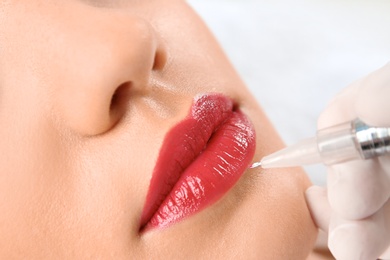 Photo of Young woman getting permanent makeup on lips in beautician salon, closeup