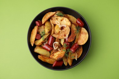 Photo of Delicious baked potato with thin dry smoked sausages, onion and dill in bowl on green table, top view