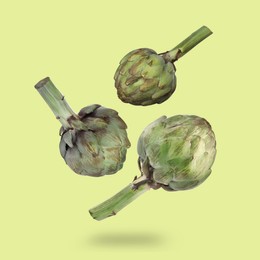 Image of Fresh raw artichokes falling on green background