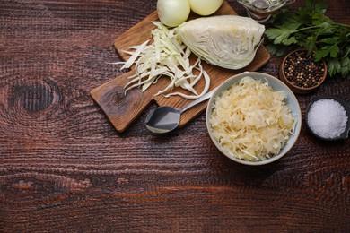 Photo of Bowl of tasty sauerkraut and ingredients on wooden table, flat lay. Space for text