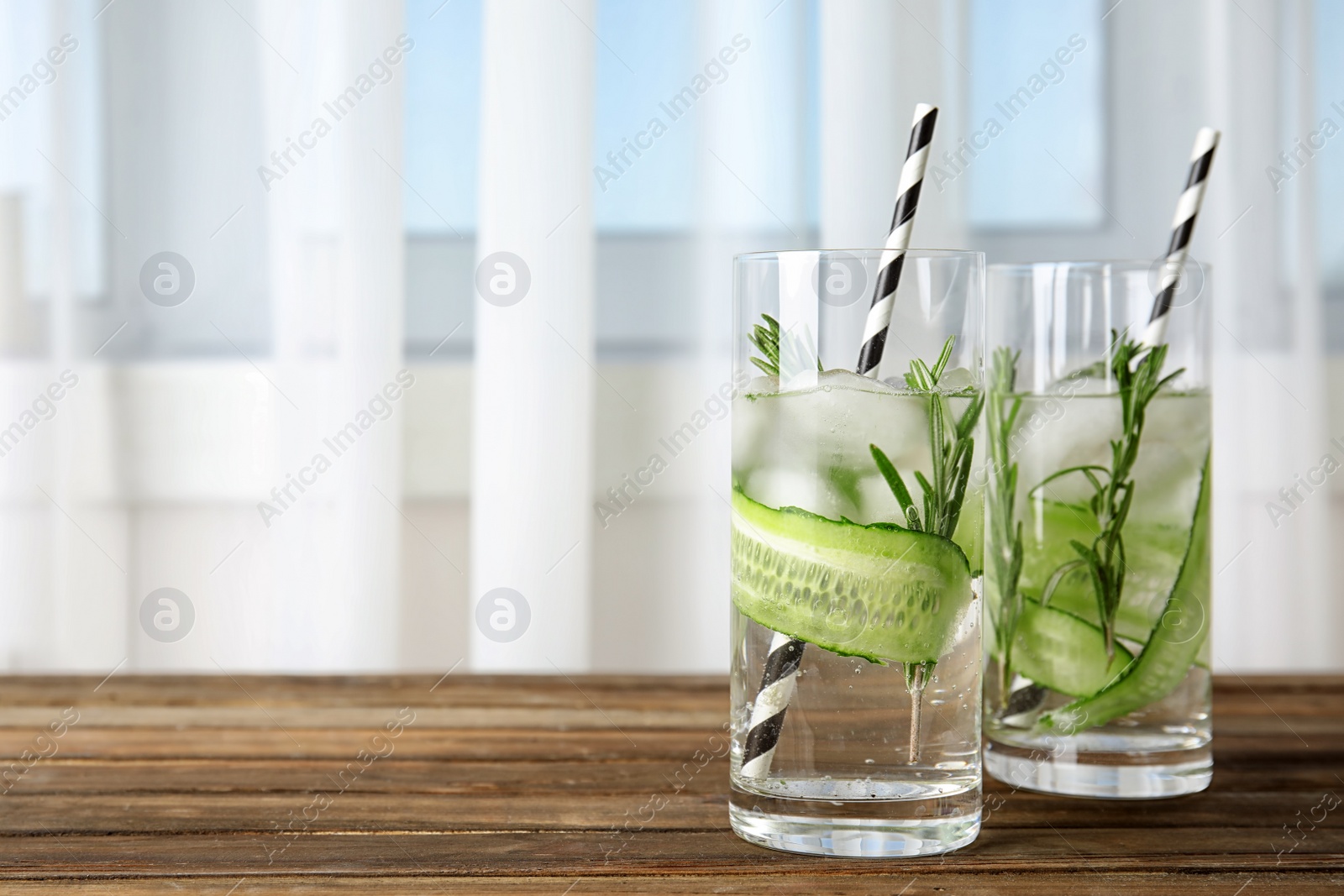 Photo of Glasses of refreshing cucumber cocktail with rosemary and space for text on blurred background