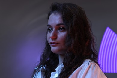 Portrait of beautiful young woman on color background with neon lights