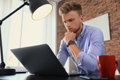 Photo of Young man using laptop at table indoors