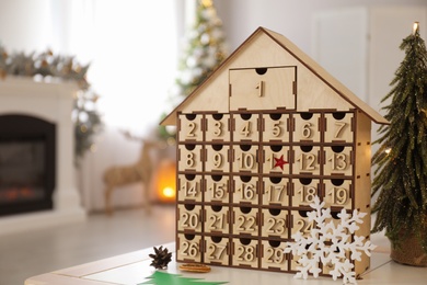 Photo of Wooden house shaped Advent calendar in room decorated for New Year