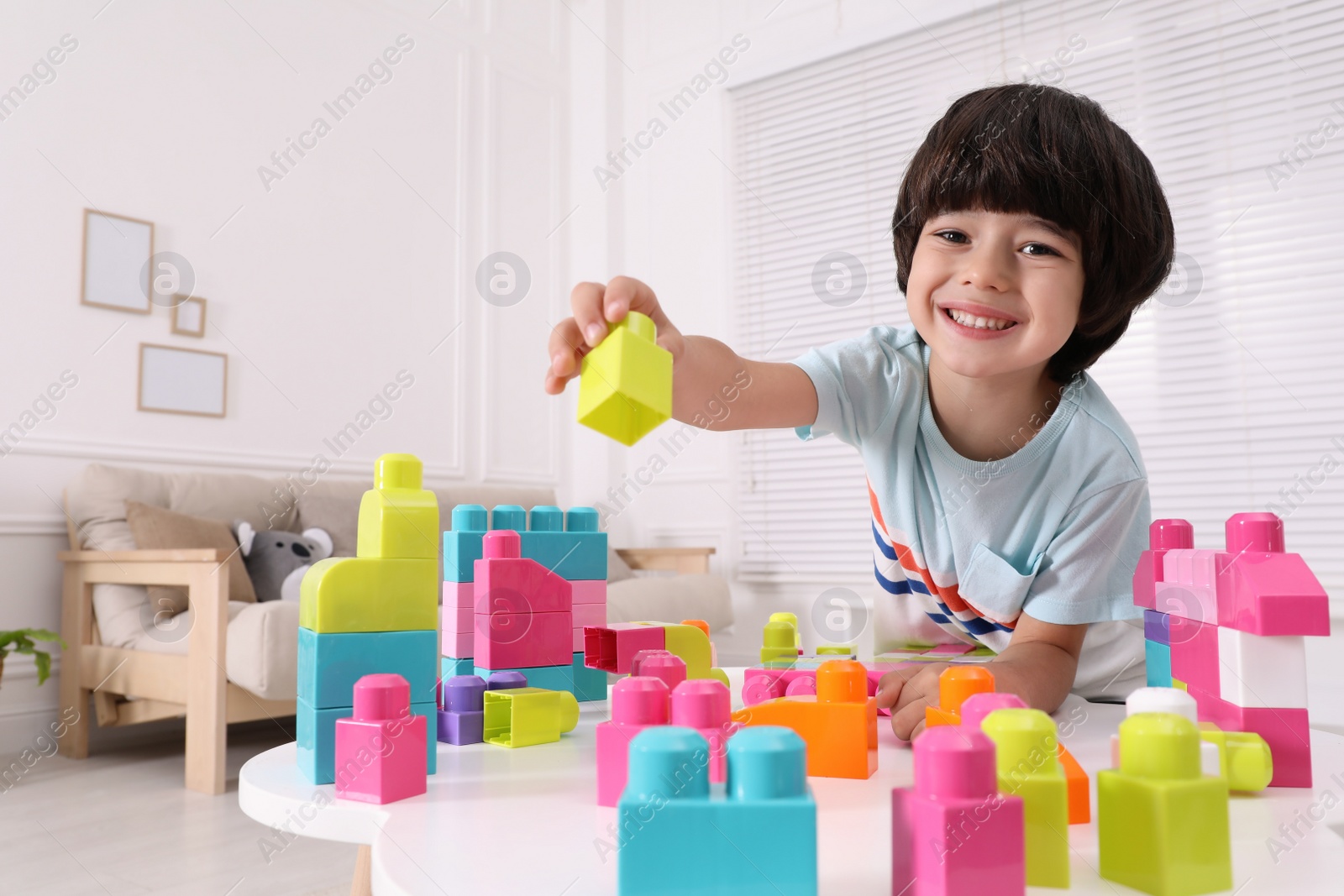 Photo of Cute little boy playing with colorful building blocks at table in living room