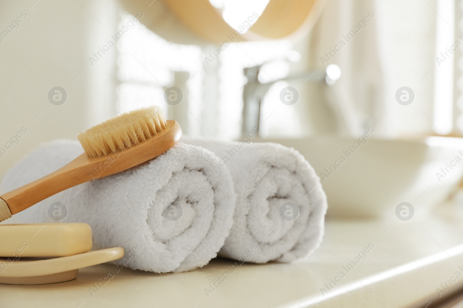 Photo of Clean rolled towels, massage brush and bar of soap on countertop in bathroom