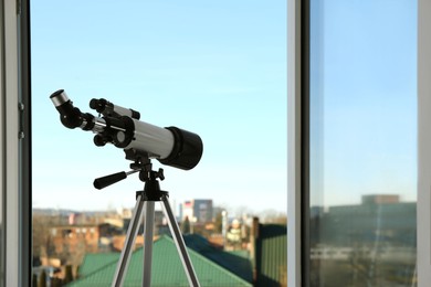 Photo of Tripod with modern telescope near open window indoors. Space for text