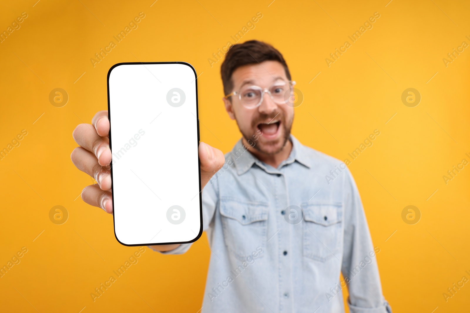 Photo of Surprised man showing smartphone in hand on yellow background, selective focus. Mockup for design