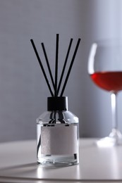 Photo of Reed diffuser and glasswine on white table indoors