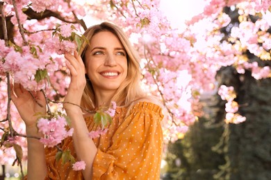 Photo of Young woman wearing stylish outfit near blossoming sakura in park. Fashionable spring look