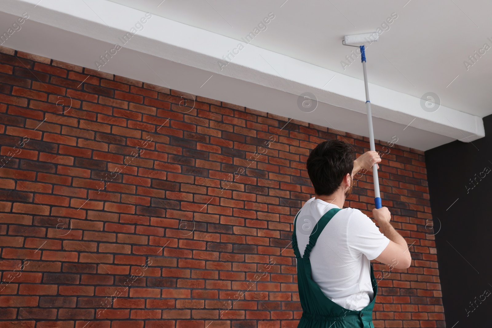 Photo of Handyman painting ceiling with roller in room, back view