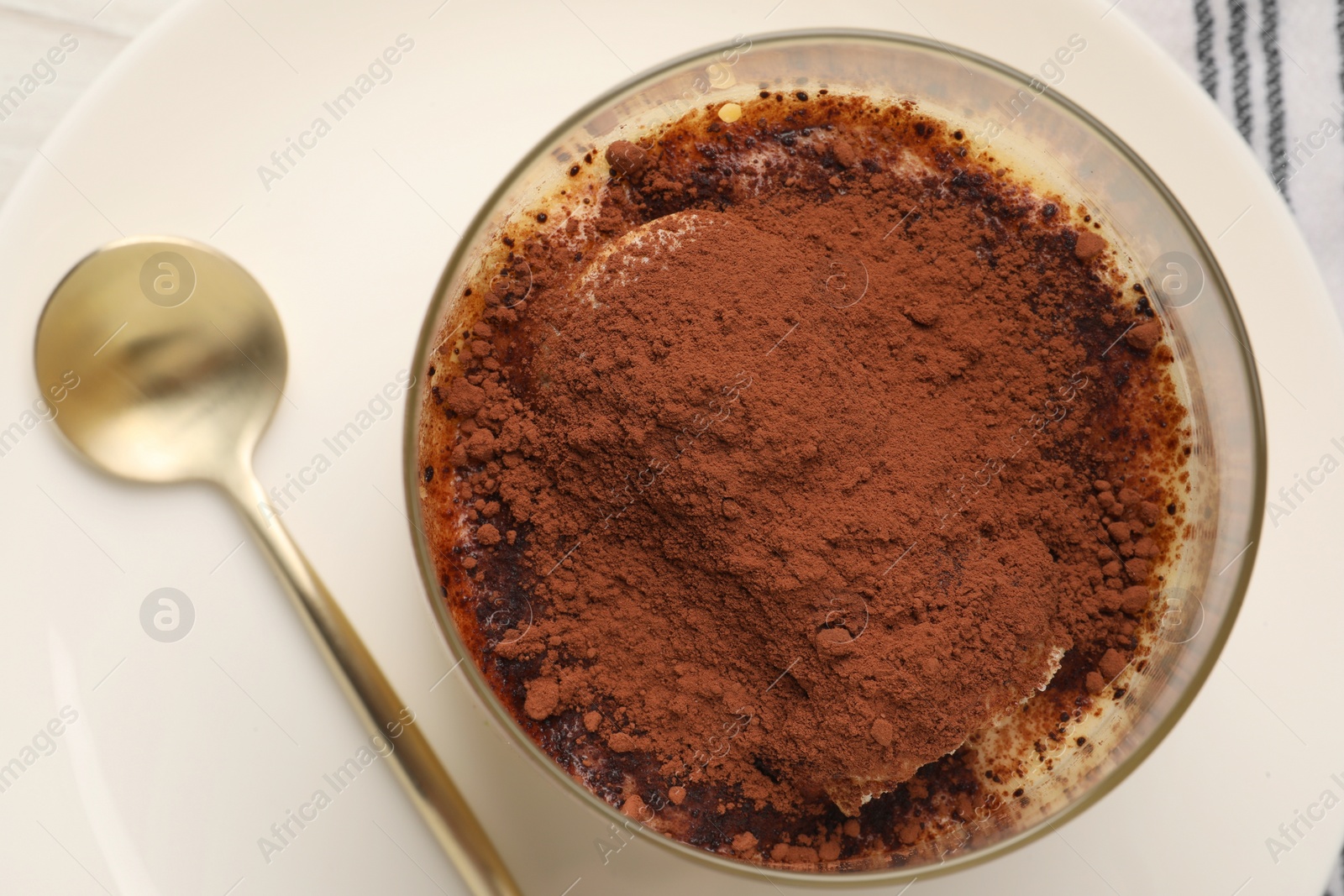 Photo of Delicious tiramisu in glass and spoon on table, top view