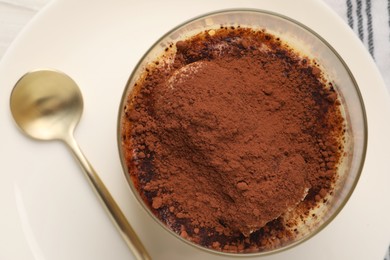 Photo of Delicious tiramisu in glass and spoon on table, top view