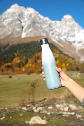 Photo of Woman holding thermo bottle with drink in mountains on sunny day