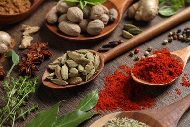 Photo of Different herbs and spices with spoons on wooden table, closeup