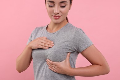 Photo of Beautiful young woman doing breast self-examination on pink background