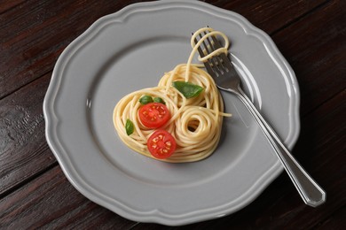 Photo of Heart made of tasty spaghetti, fork, tomato and basil on wooden table