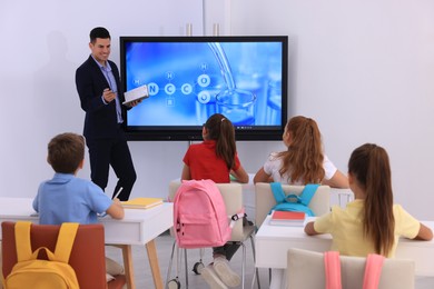 Photo of Teacher giving lesson to pupils near interactive board in classroom