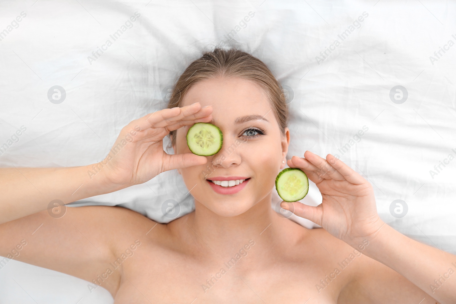 Photo of Beautiful woman with cucumber slices on white fabric, above view. Organic face mask