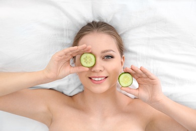 Photo of Beautiful woman with cucumber slices on white fabric, above view. Organic face mask