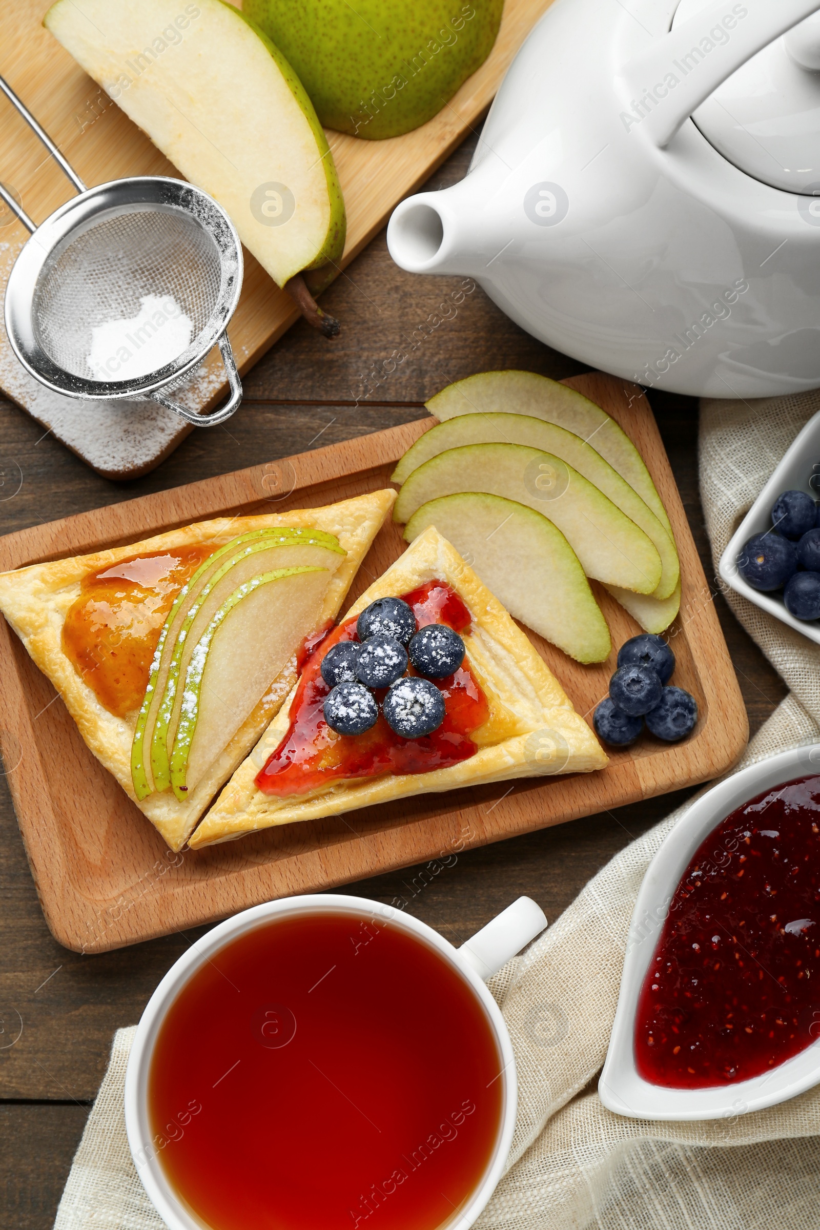 Photo of Fresh tasty puff pastry with jam, blueberries and pear served on wooden table, flat lay