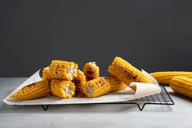 Cooling rack with grilled corn cobs on table against gray background