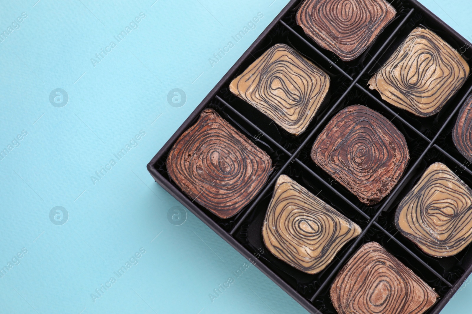 Photo of Box of tasty chocolate candies on light blue background, top view. Space for text