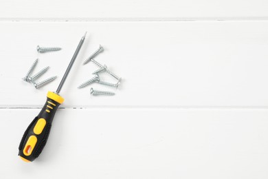 Photo of Screwdriver with black handle and screws on white wooden table, flat lay. Space for text