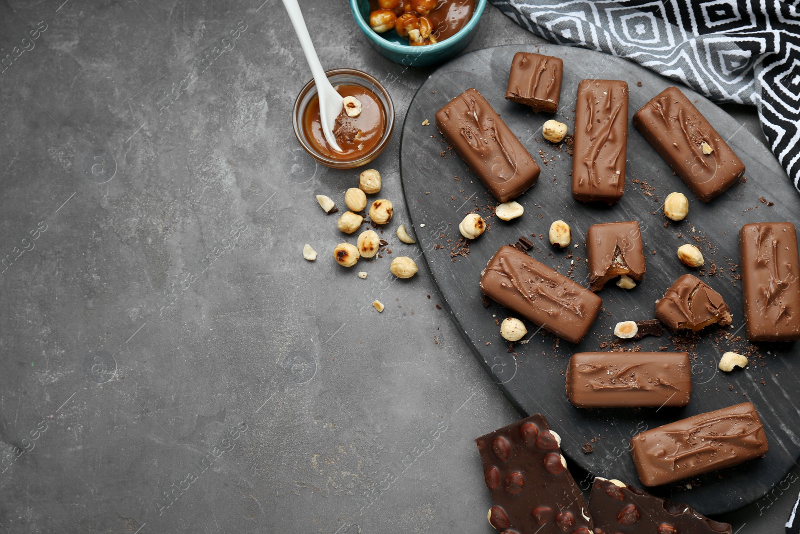 Photo of Delicious chocolate candy bars with caramel and nuts on grey table, flat lay. Space for text