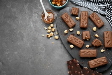Photo of Delicious chocolate candy bars with caramel and nuts on grey table, flat lay. Space for text