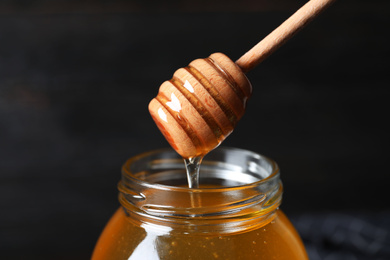 Photo of Jar of organic honey and dipper on dark background, closeup