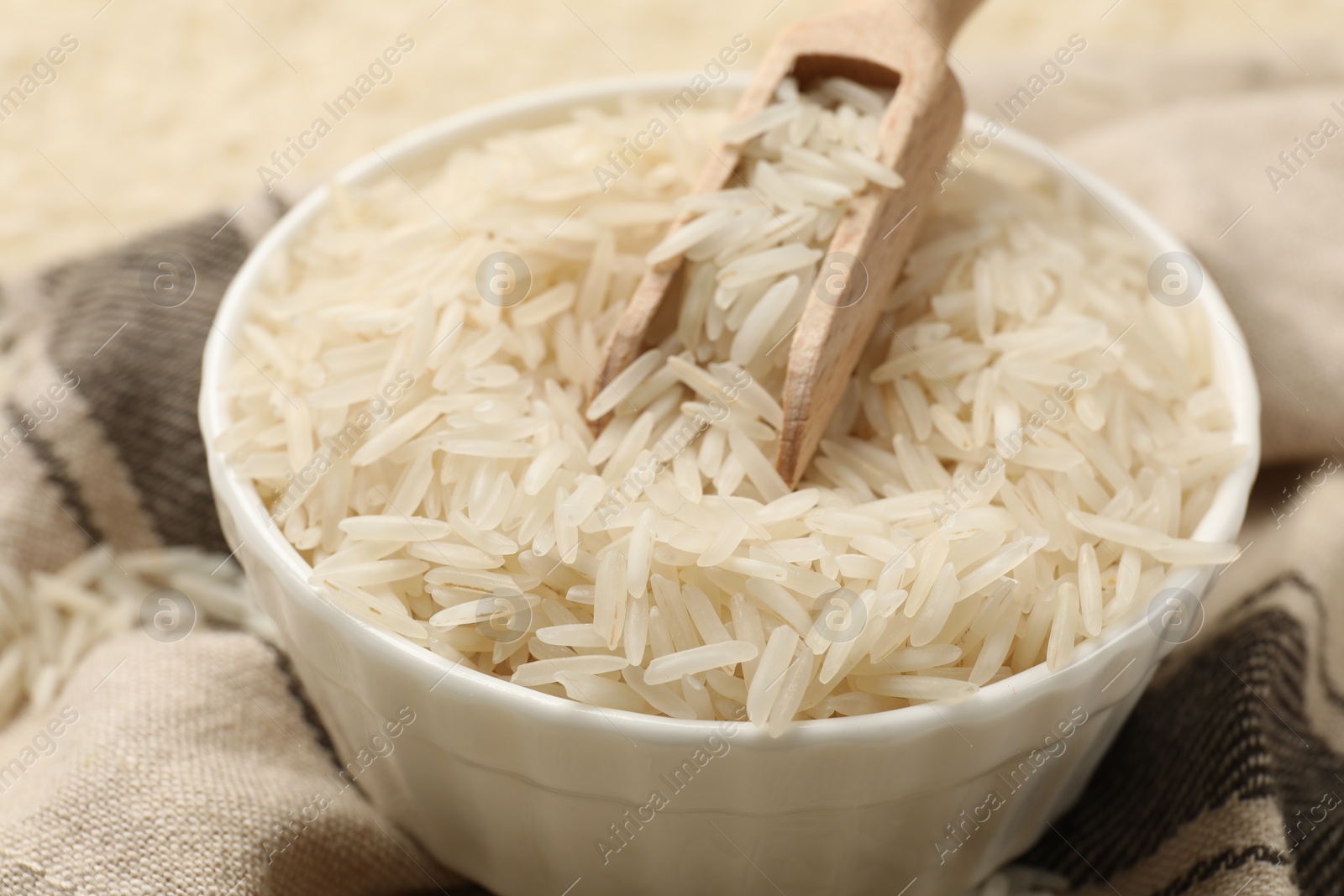 Photo of Raw basmati rice in bowl and scoop on cloth, closeup