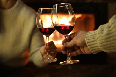 Photo of Couple clinking glasses of wine near fireplace at home, closeup
