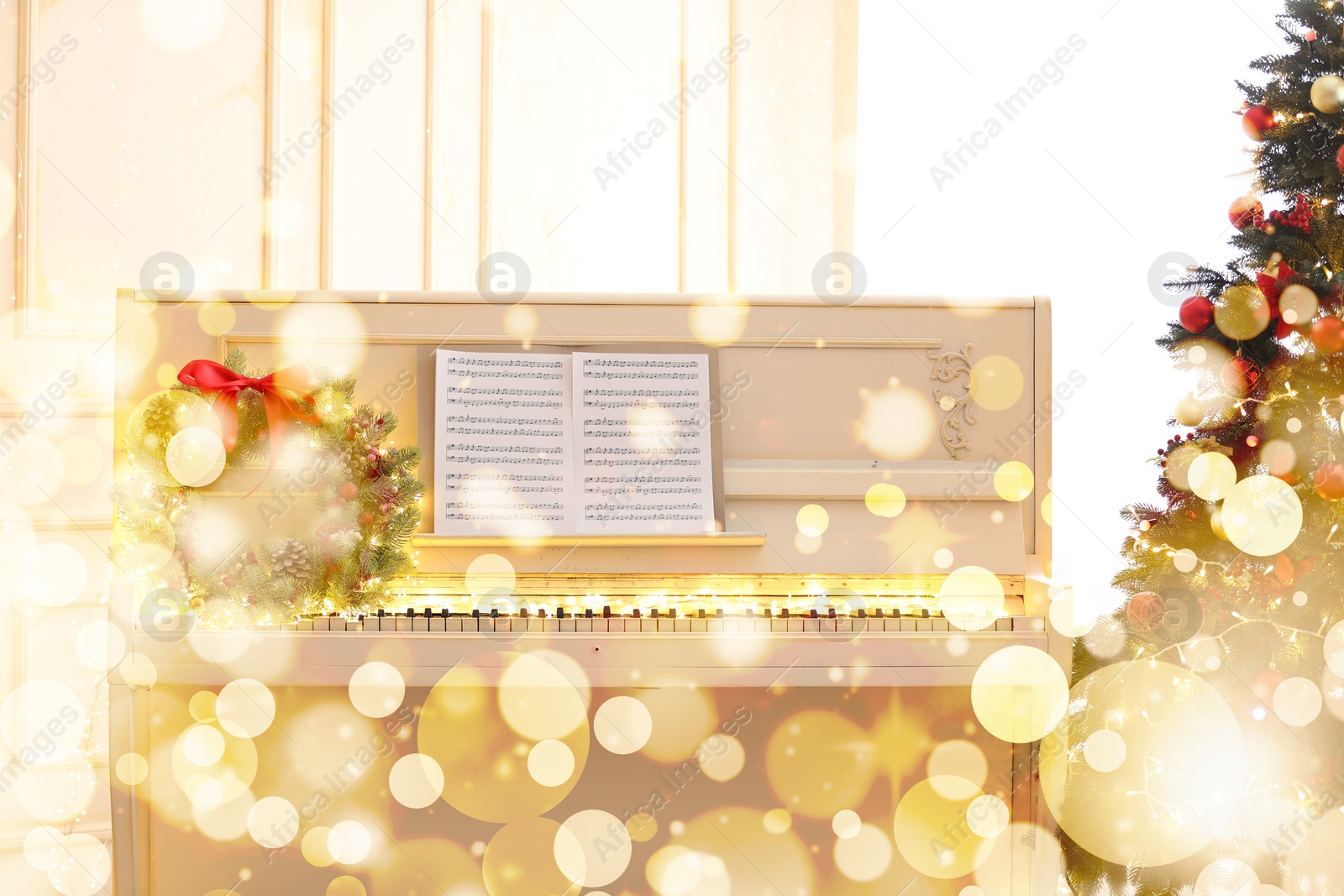 Image of Winter holidays music. Piano with festive wreath near Christmas tree, bokeh effect