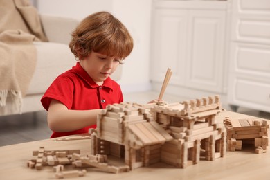 Cute little boy playing with wooden castle at table in room. Child's toy