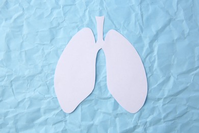 Photo of Paper in shape of human lungs on light blue crumpled background, top view