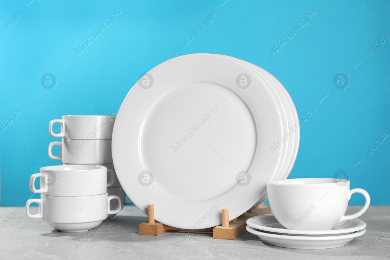 Photo of Set of clean dishware on grey table against light blue background