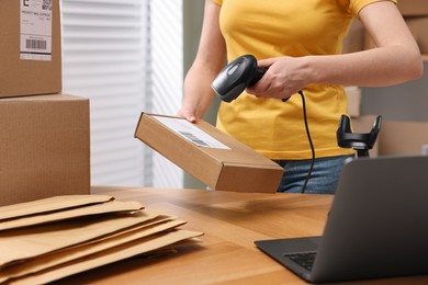 Parcel packing. Post office worker with scanner reading barcode at wooden table indoors, closeup