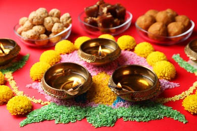 Photo of Happy Diwali. Diya lamps, colorful rangoli, flowers and delicious Indian sweets on red table, closeup