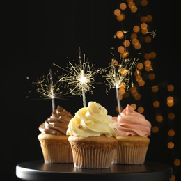 Birthday cupcakes with sparklers on stand against dark background
