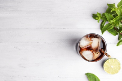Photo of Glass of refreshing soda drink with ice cubes, mint and lime on white wooden table, flat lay. Space for text