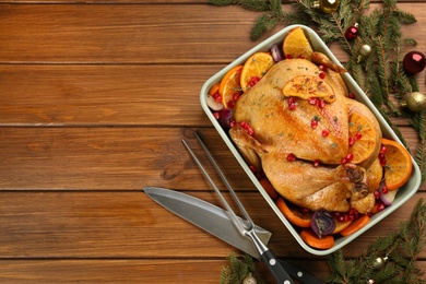 Photo of Roasted chicken with oranges, pomegranate and vegetables near fir tree branches on wooden table, flat lay. Space for text