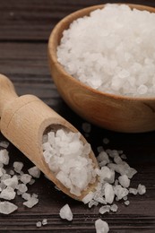 Photo of Bowl and scoop with sea salt on wooden table, closeup