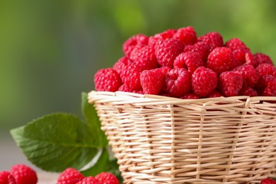 Photo of Wicker basket with tasty ripe raspberries on blurred green background, closeup