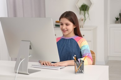 Cute girl using computer at desk in room. Home workplace