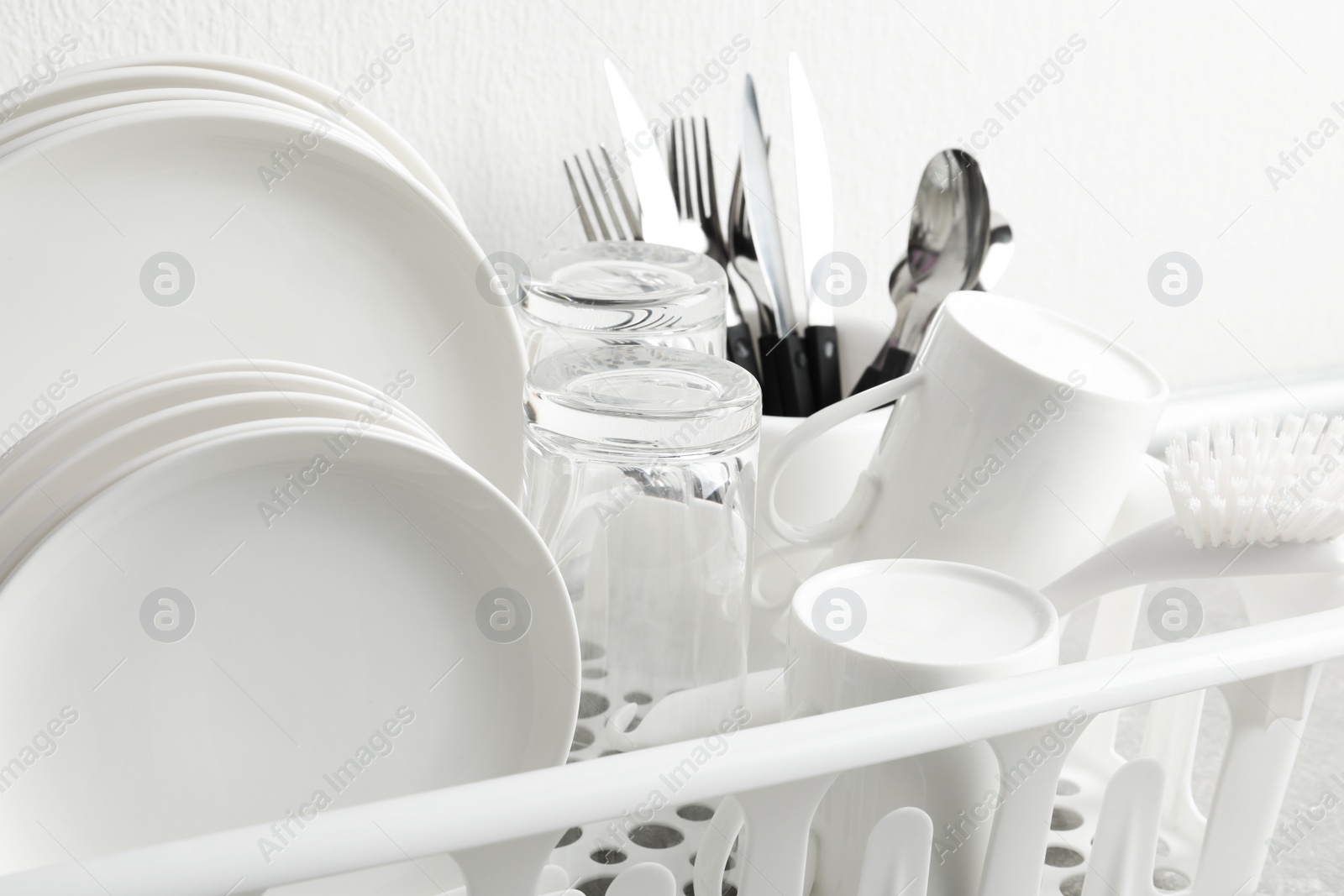 Photo of Drying rack with clean dishes and cutlery near white wall